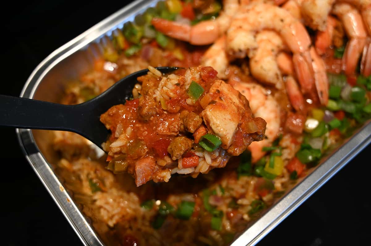 Closeup image of the tray of jambalaya cooked with a big spoon scooping some out.