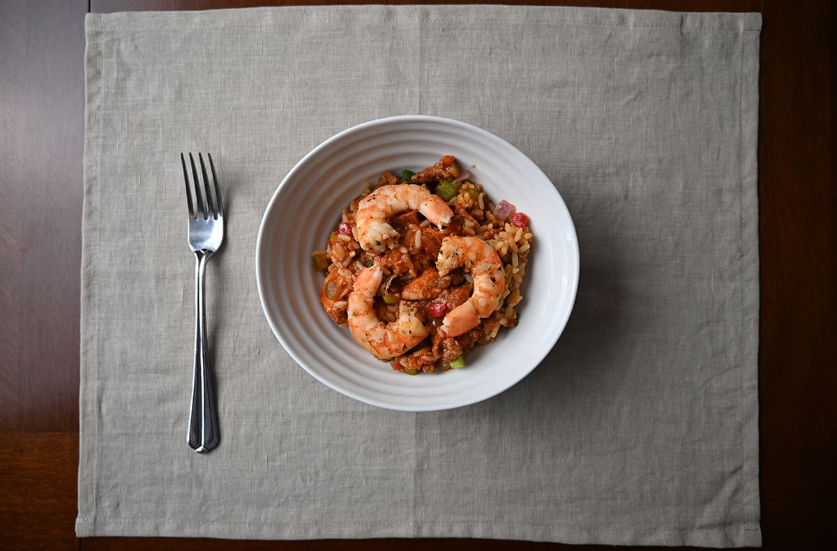 Top down image of a bowl of jambalaya with shrimp on it sitting beside a fork.