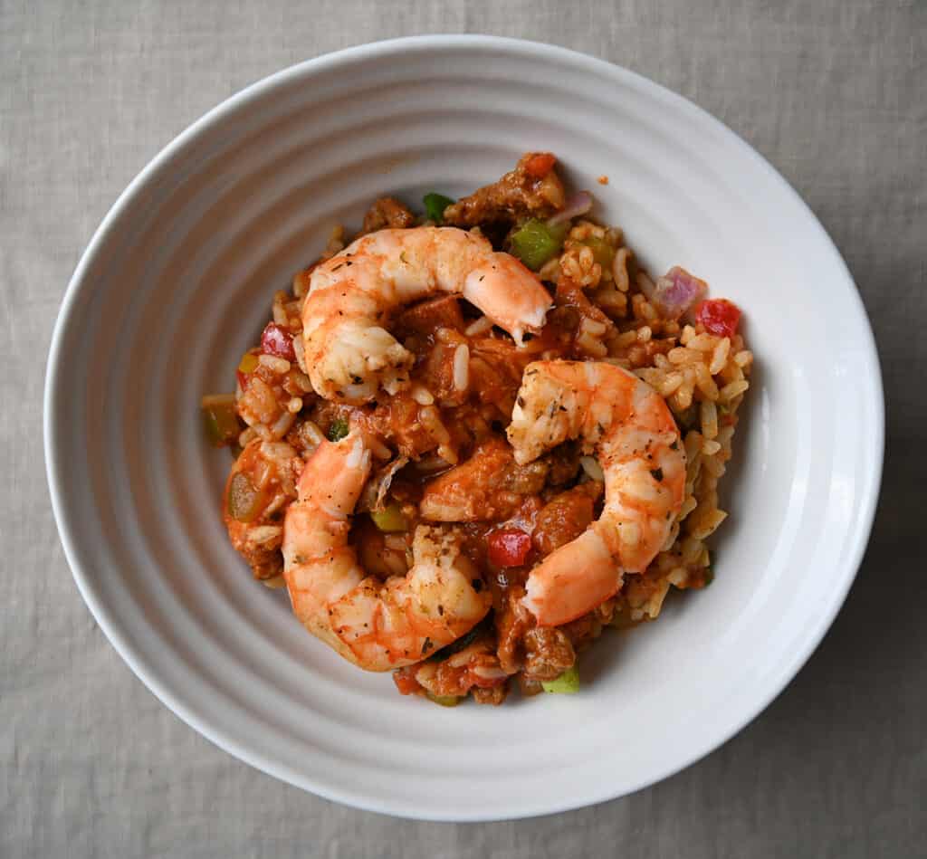 Top down closeup image of a bowl of jambalaya with three shrimp resting on top of the rice stew.