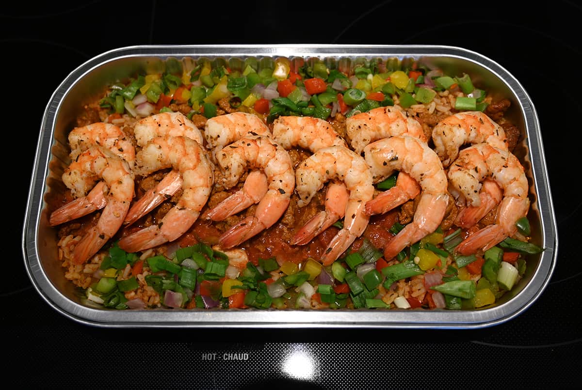 Top down image of the jambalaya container opened sitting on a table, there are shrimp resting on top of the jambalaya.