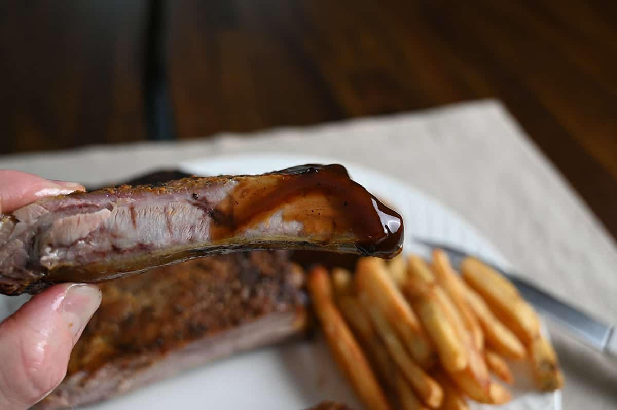 Closeup image of a hand holding one rib dipped in barbecue sauce.