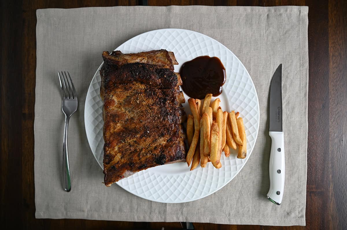 Top down image of a slab of ribs served on a white plate beside some fries and barbecue sauce. 