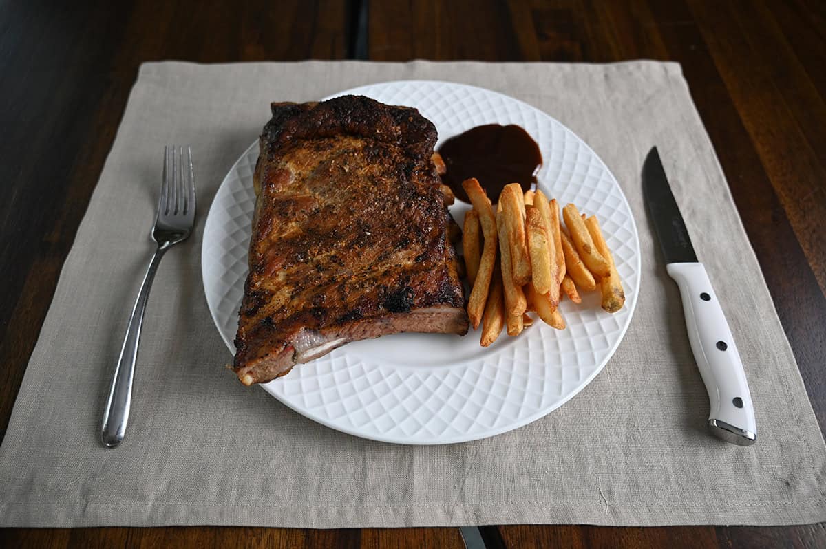 Sideview top down image of a large slab of ribs beside a side of fries served on a white plate.
