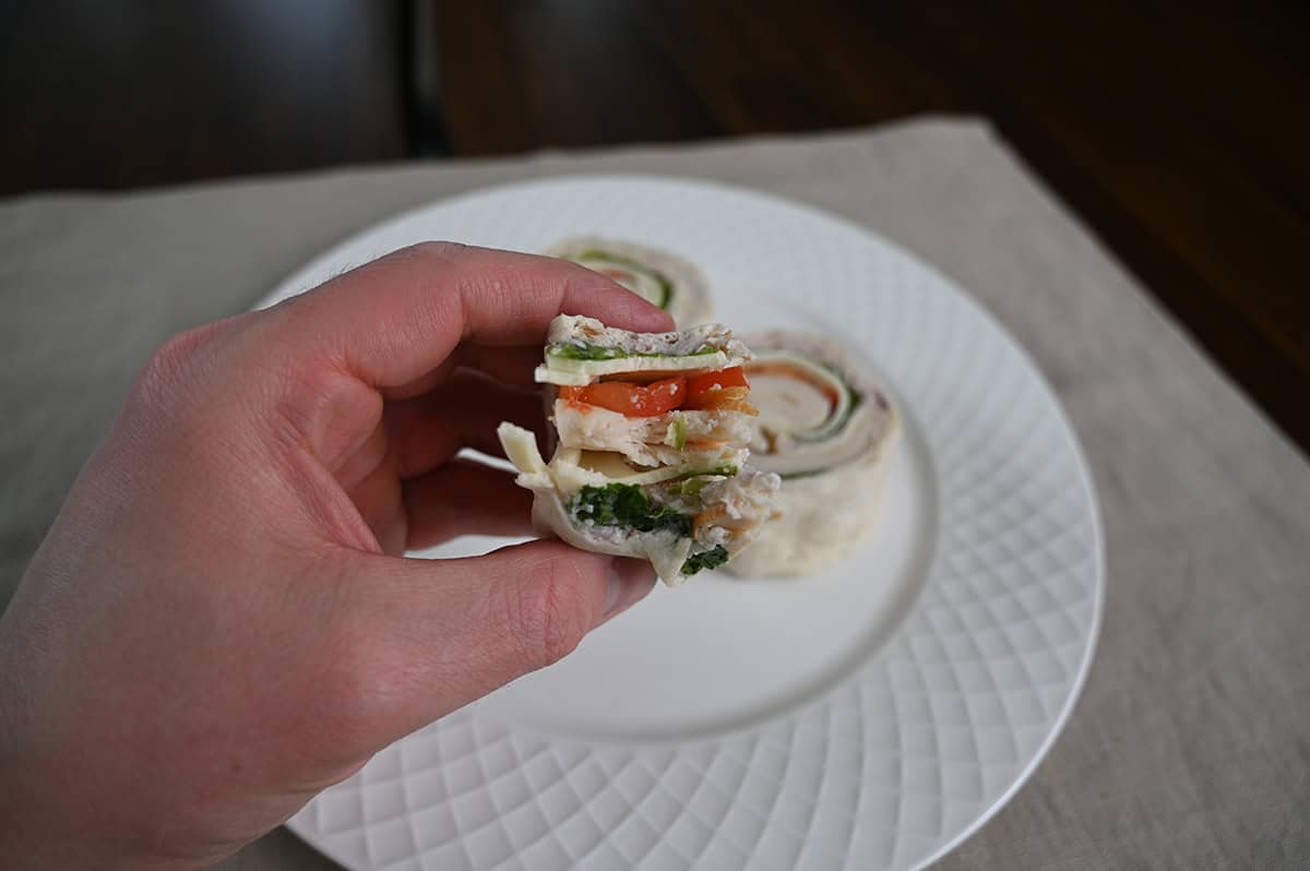 Image of a hand holding on wrap roll with a few bites taken out of it, you can see the tomatoes, lettuce, cheese and chicken.