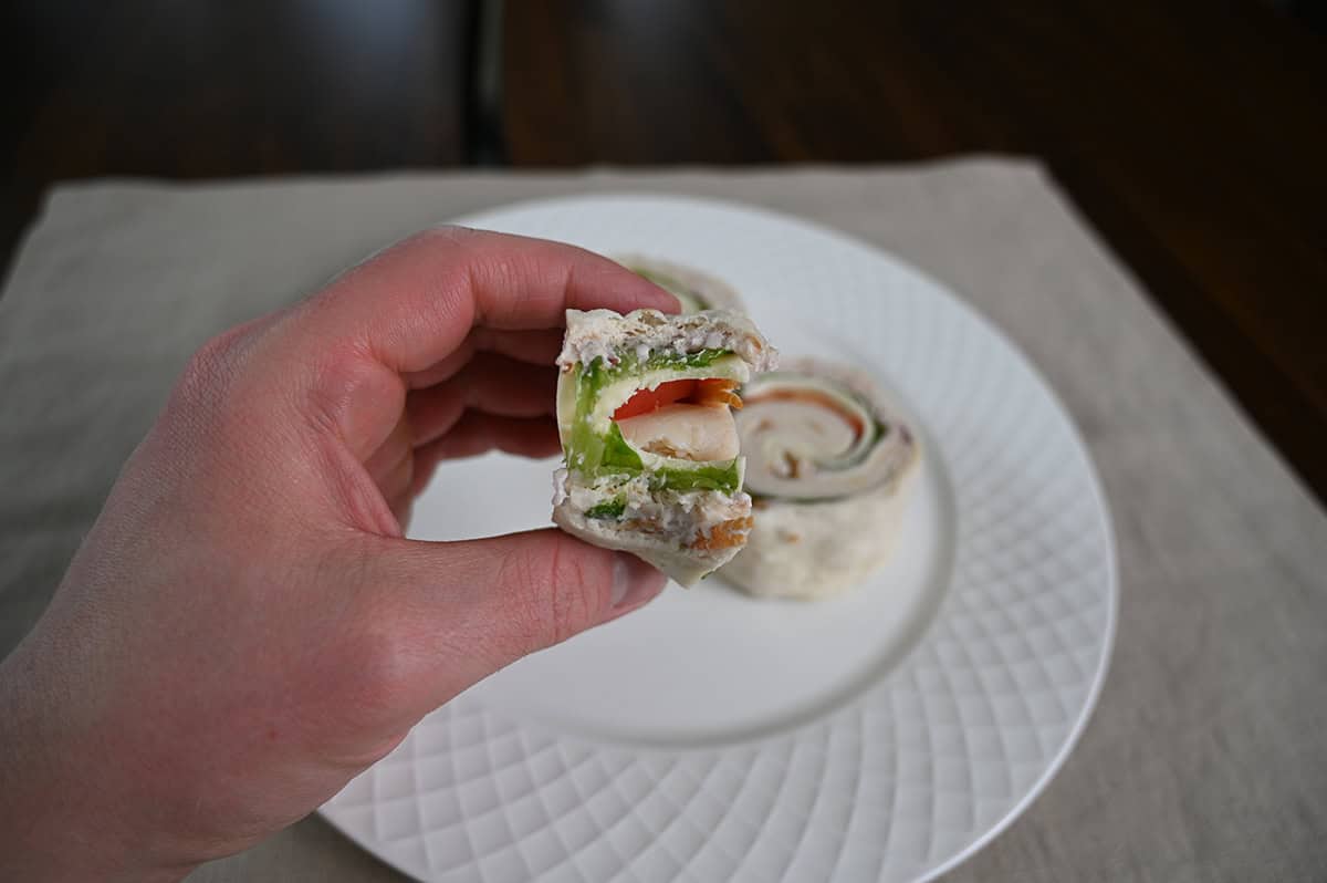 Image of a hand holding on wrap roll with a few bites taken out of it, you can see the tomatoes, lettuce, cheese and chicken.