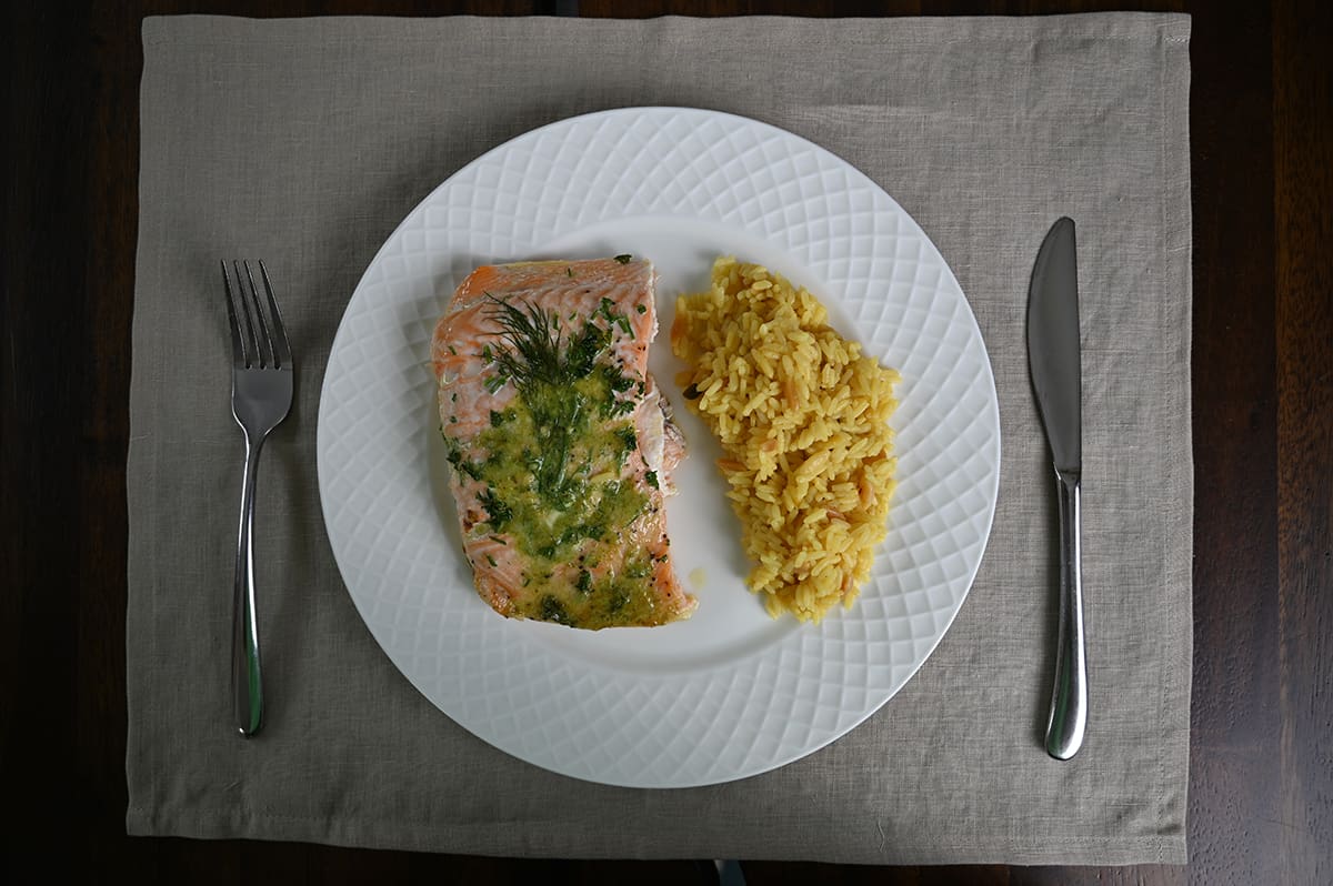 Top down image of one large piece of cooked salmon served on a white plate beside a side of couscous.