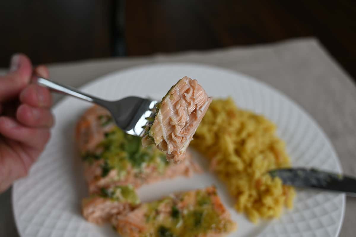 Closeup image of a fork with a bite of salmon on it, in the background of the image is a plate with a piece of salmon on it and couscous.