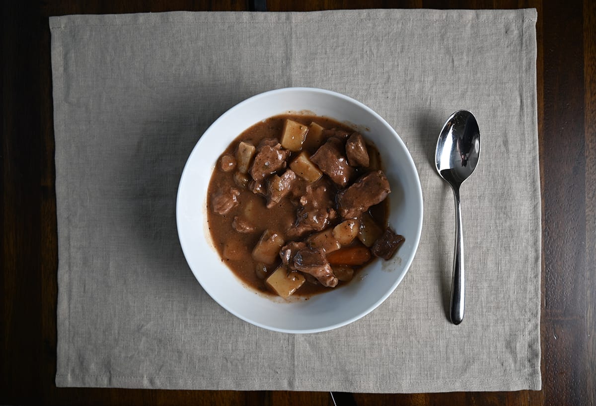 Top down image of a bowl of stew served beside a spoon.