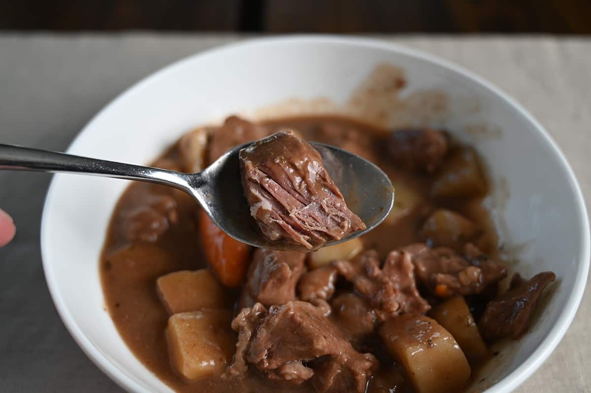 Closeup image of a spoon with a piece of beef on it hovering over a bowl.
