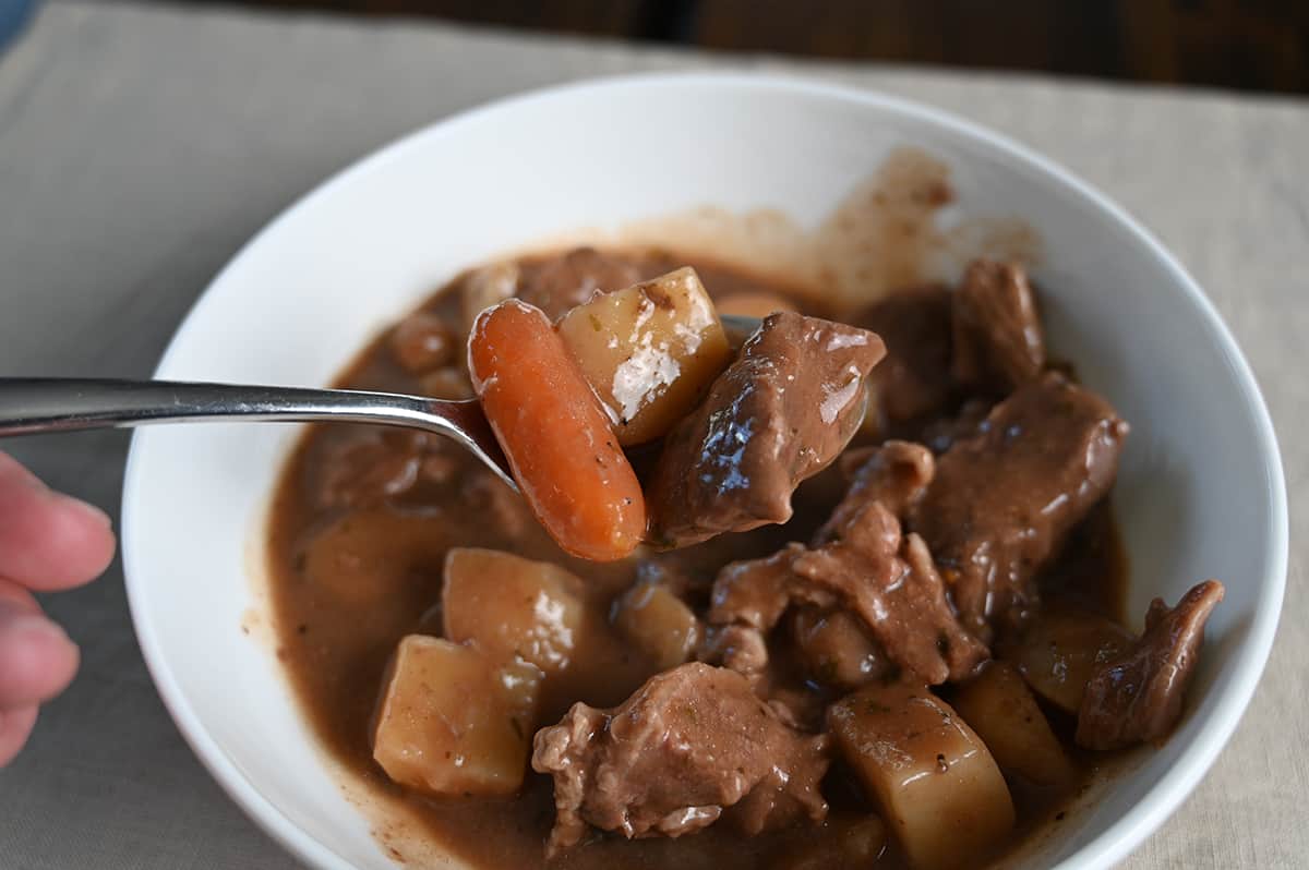 Closeup image of a spoon with carrots, potatoes and beef on it hovering over a bowl of stew.
