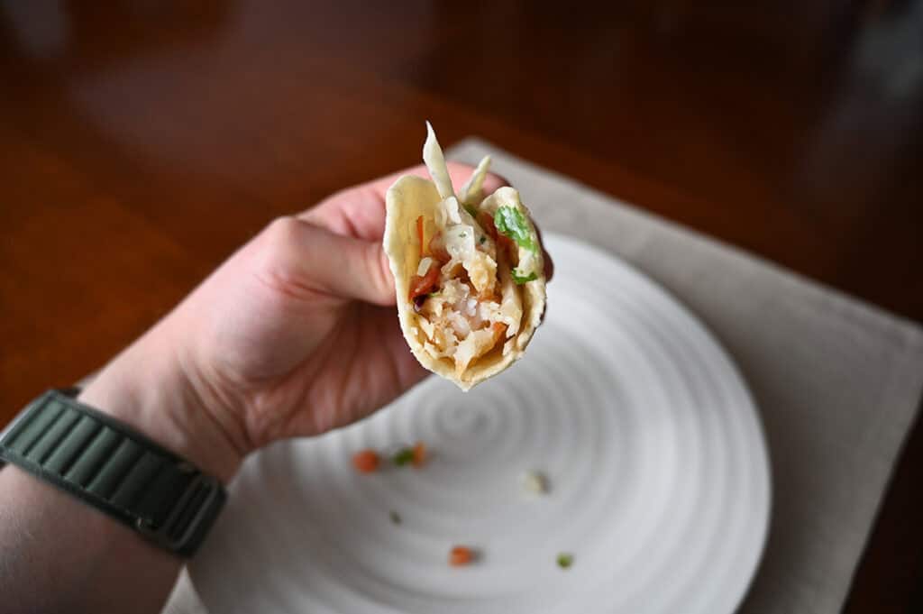 Sideview image of a hand holding one taco close to the camera with a few bites taken out of it so you can see the filling.