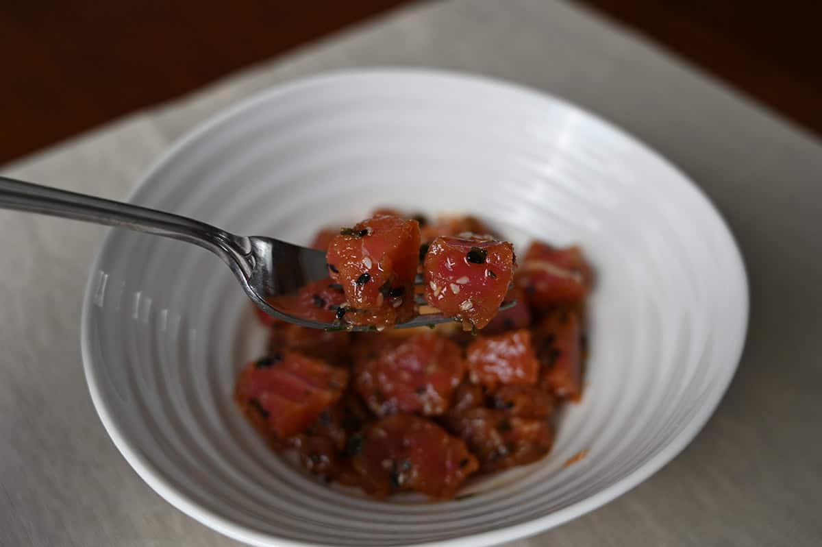 Closeup image of a fork with a piece of tuna poke on it with a bowl in the background.