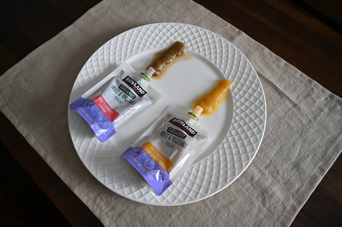 Side view top down image of both flavors of pouches laying on a white plate, the pouches have been squeezed out onto the plate so you can see what the puree looks like.