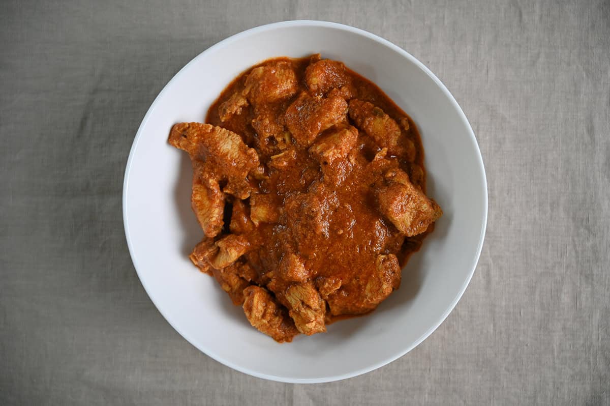 Top down closeup image of a bowl of tikka masala, there are large chunks of chicken visible with sauce.