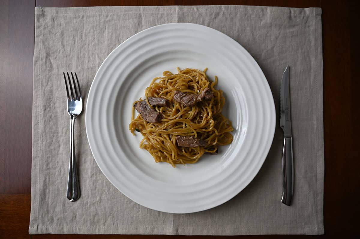 Top down image of a plate of beef noodle stir fry with a fork and knife resting beside the plate.