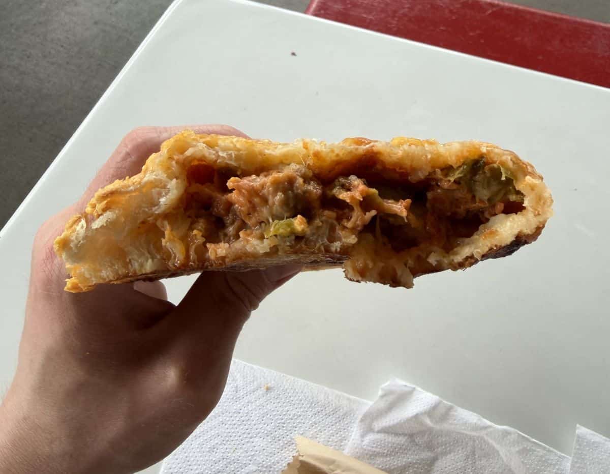 Image of the Costco Food Court Calzone close to the camera with a few bites taken out of it so you can see all the filling inside.