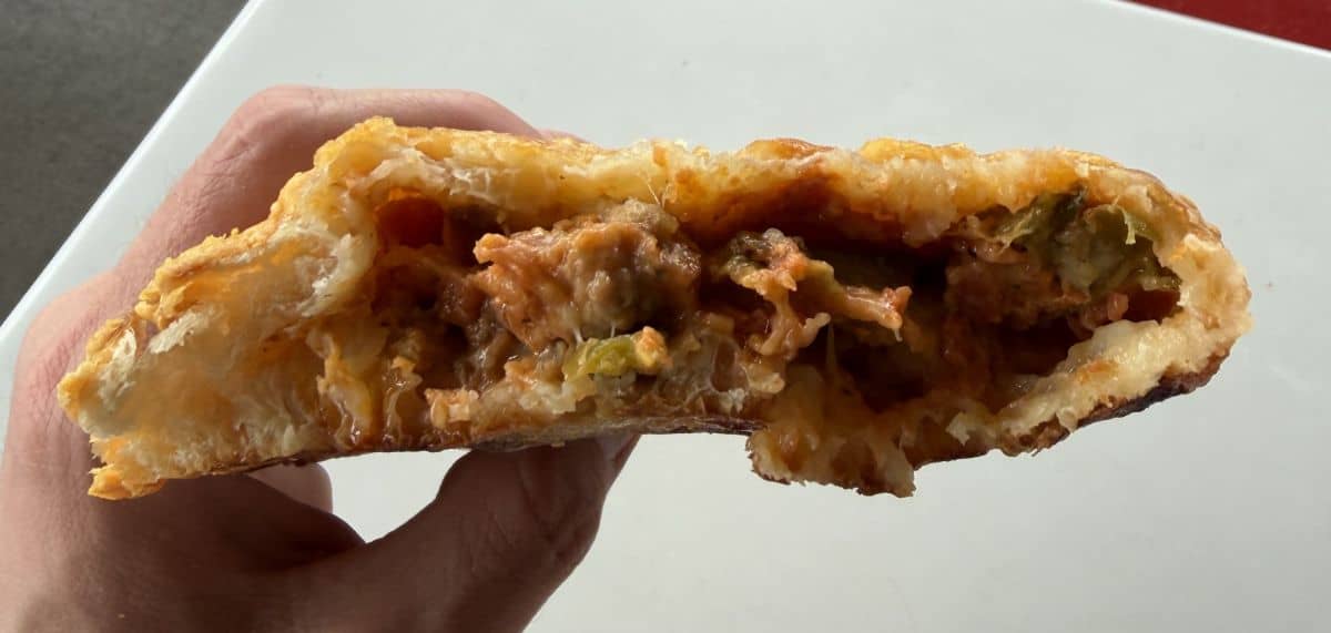 Image of a hand holding the calzone close to the camera with bites taken out of it so you can see the filling.