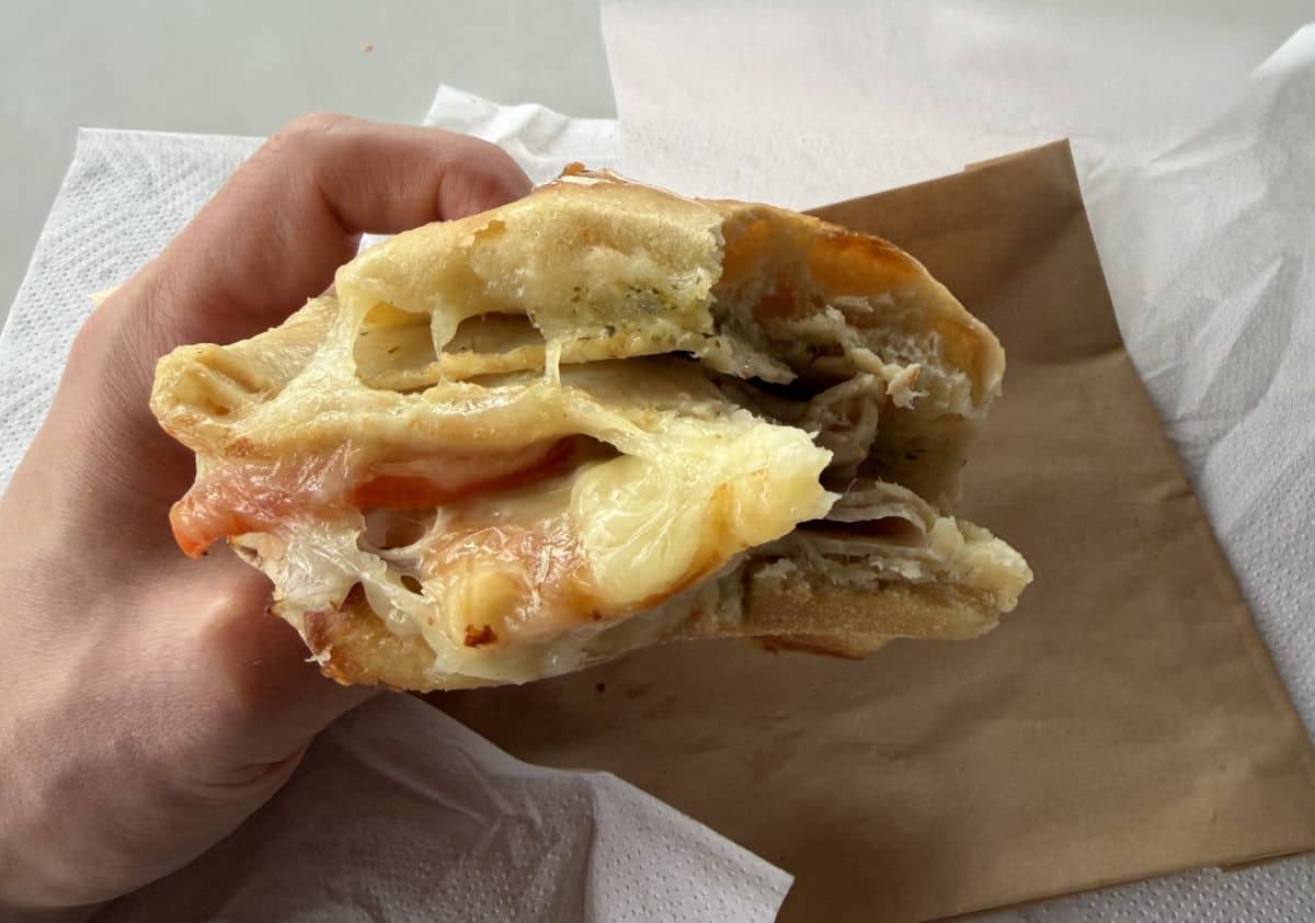 Closeup image of the Hot Turkey & Provolone Sandwich from Costco with a few bites taken out of it showing the cheesy, meaty, filling.