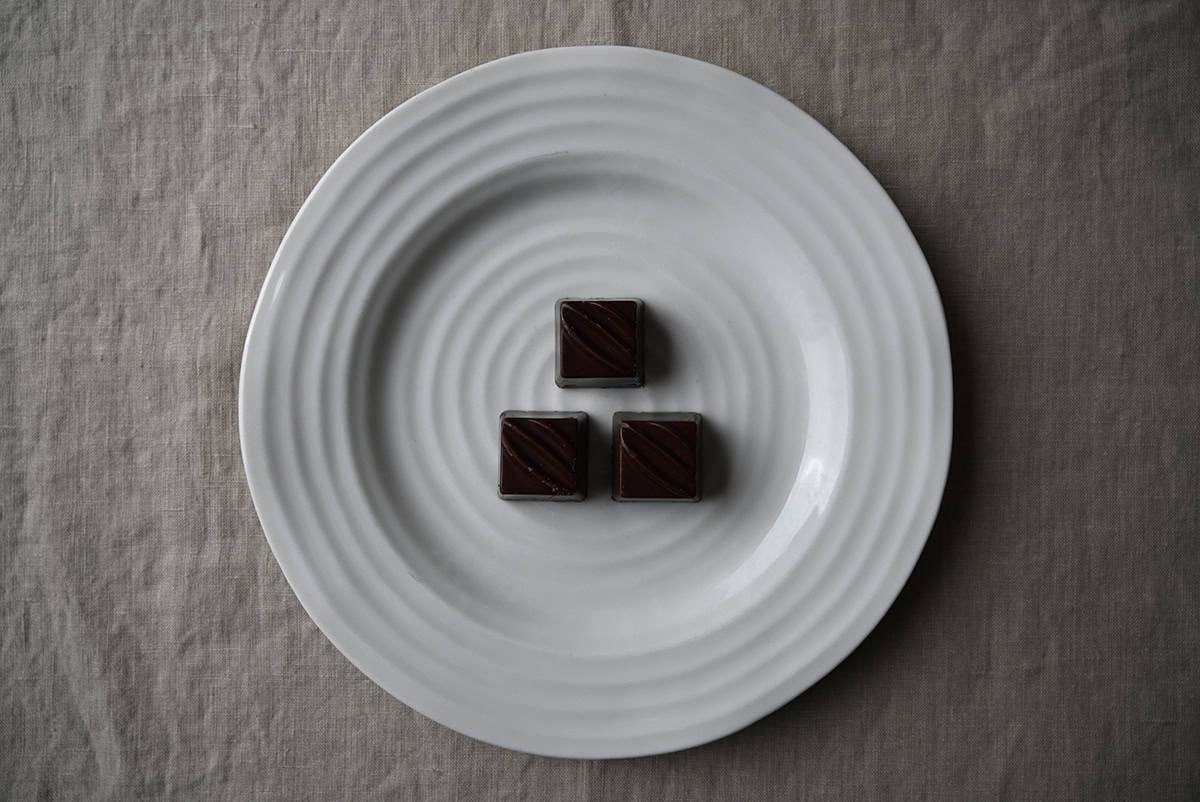 Image of three dark chocolate truffles served on a white plate.