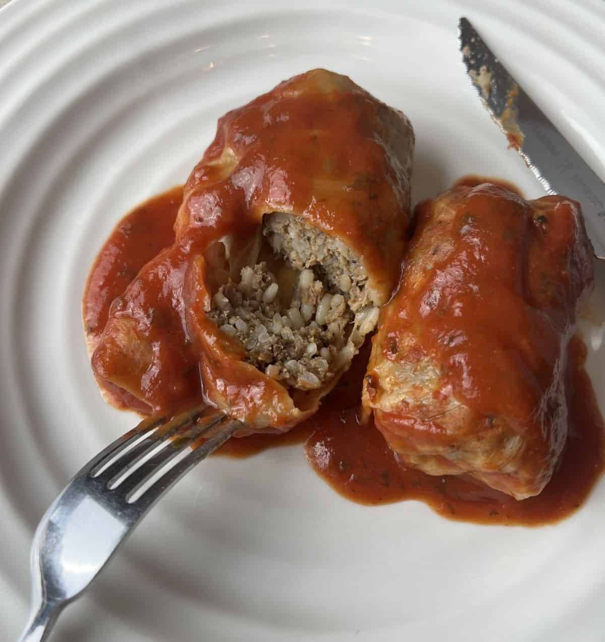 Closeup image of a cabbage roll on a plate cut into so you can see the rice and beef on the inside.