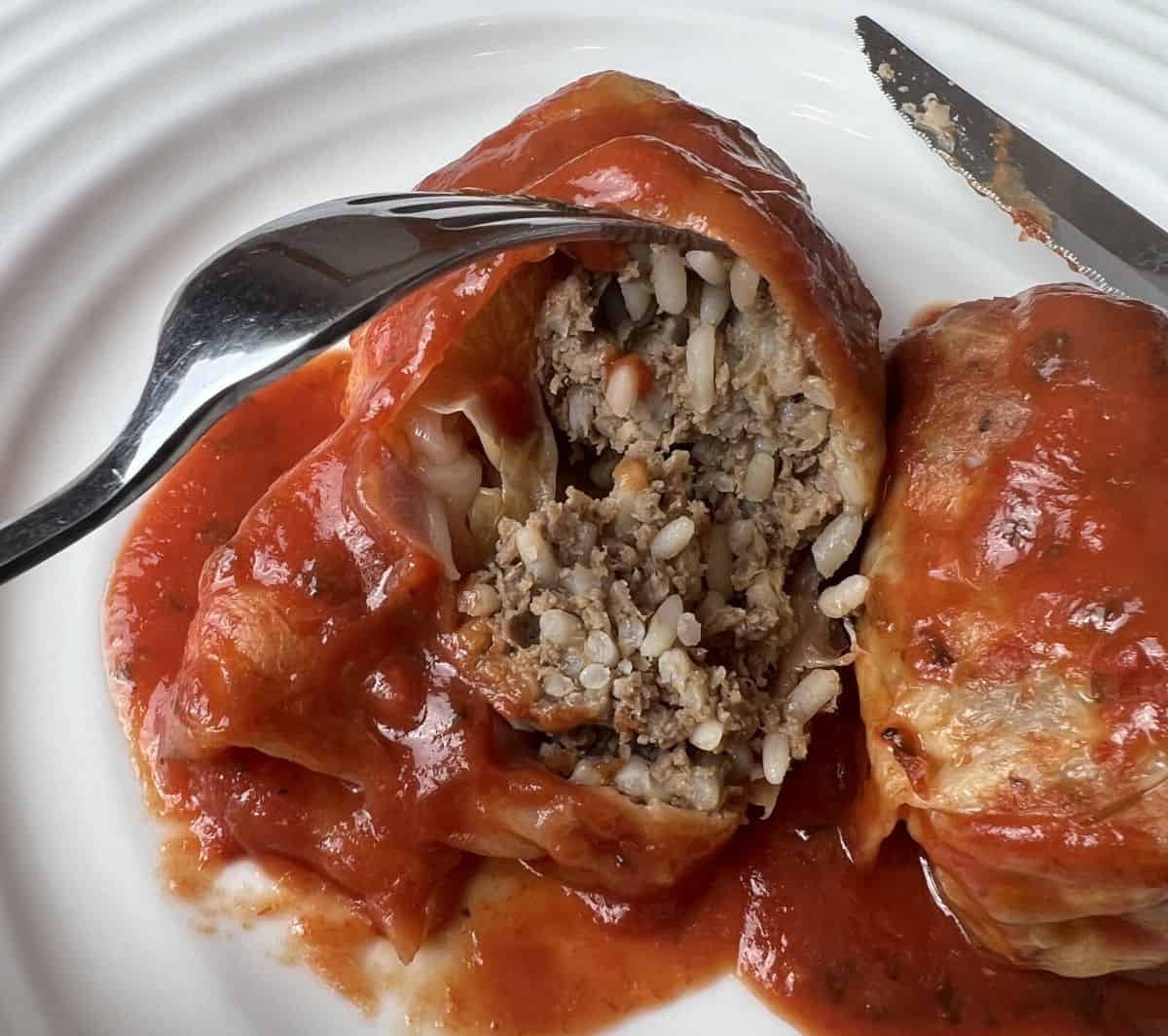 Closeup image of a cabbage roll on a white plate cut into so you can see the filling.