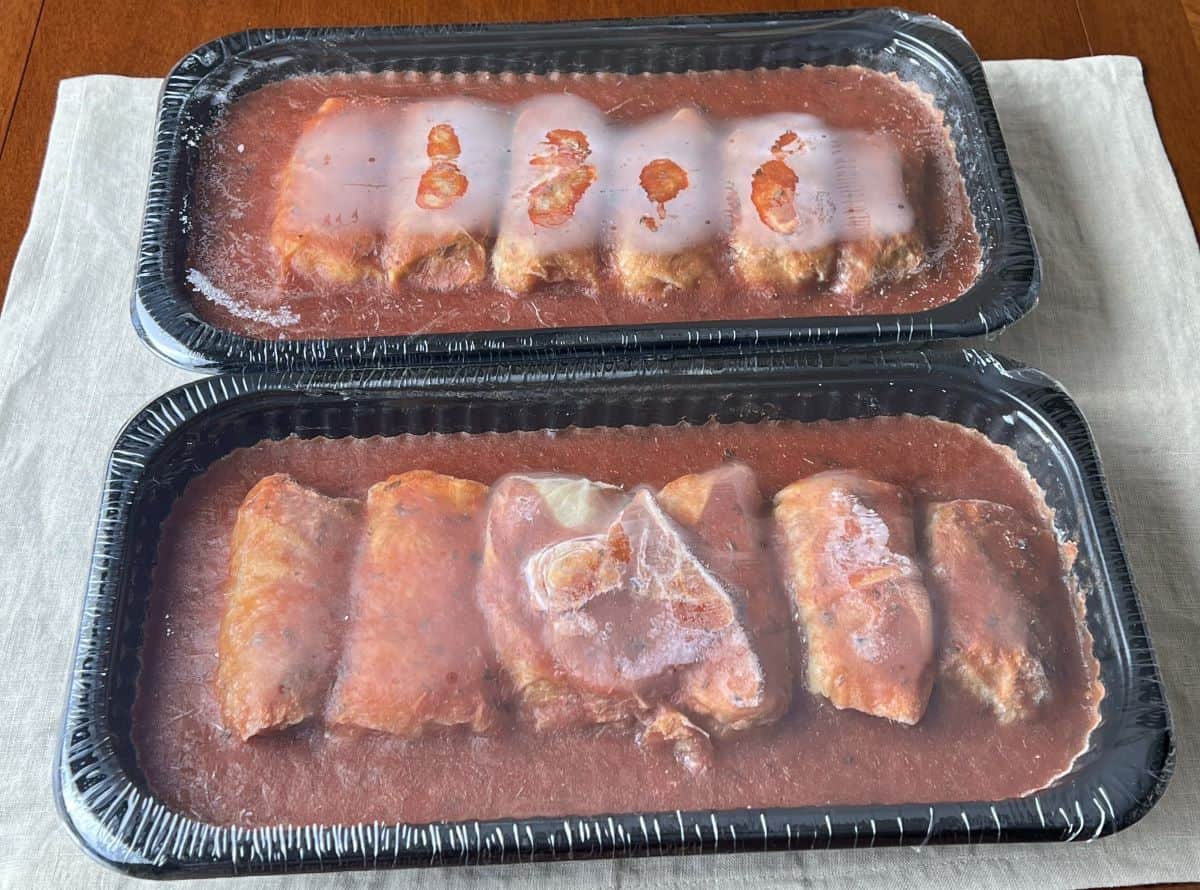 Image of two trays of frozen cabbage rolls sealed with plastic wrap on top.