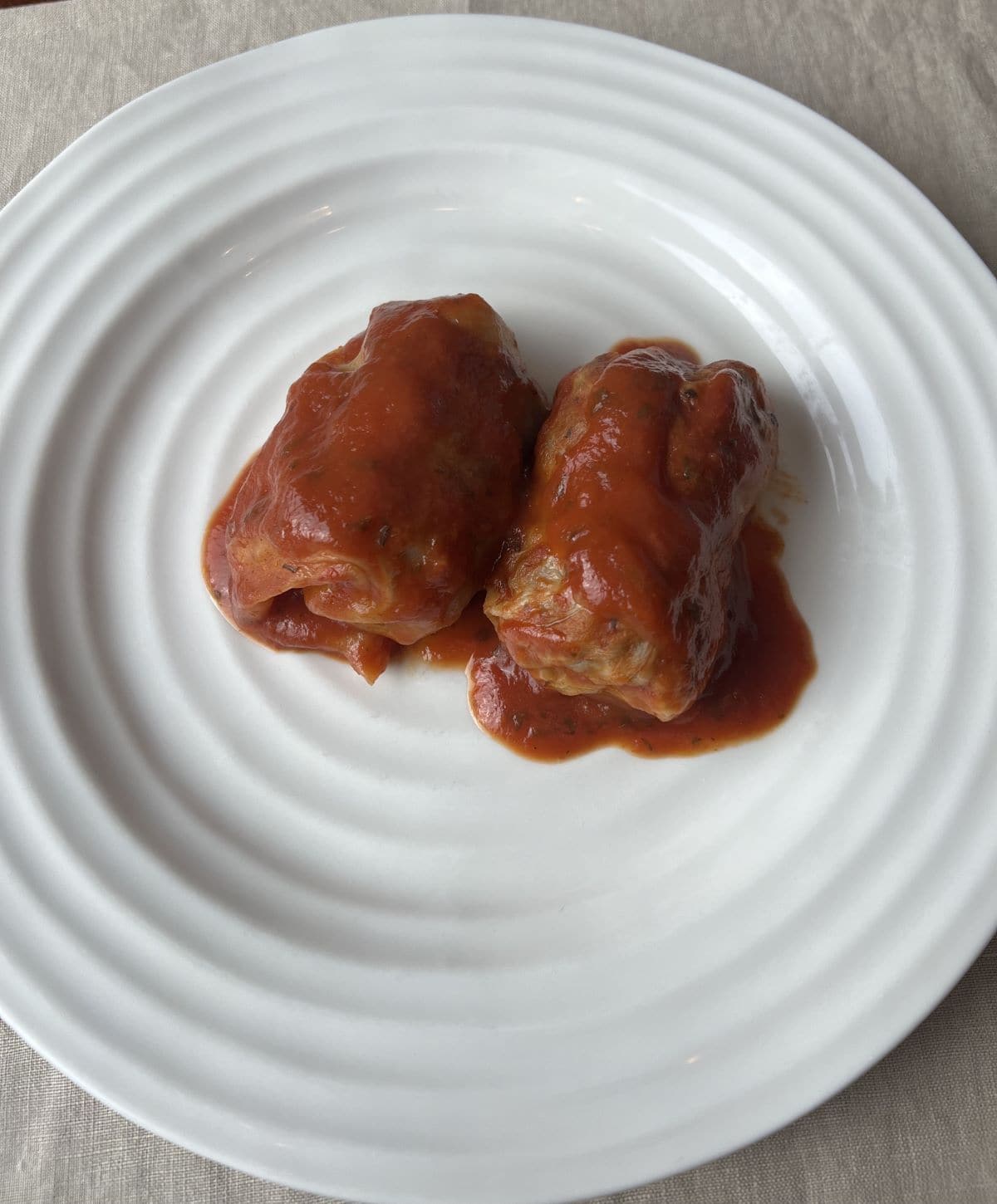 Closeup image of two cabbage rolls served on a white plate with tomato sauce on top.