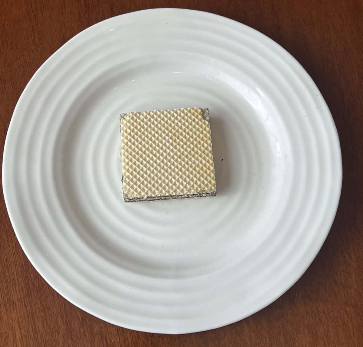 Top down image of one wafer cookie served on a white plate.