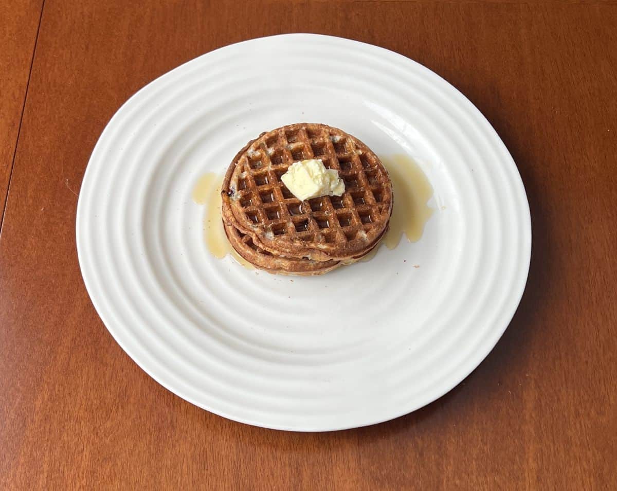 Top down image of two Brazi Bites waffles served on a white plate with butter and syrup. 