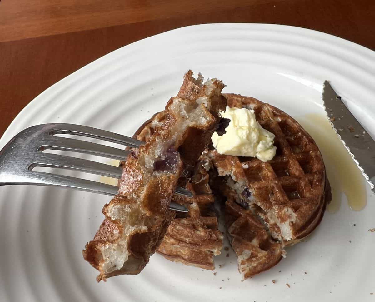 Image of a fork with a bite of Brazi Bite waffle on it hovering over a plate of waffles.