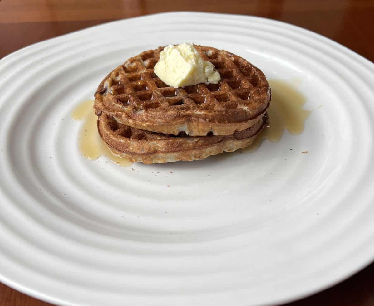 Image of two waffles served on a white plate with syrup and butter.