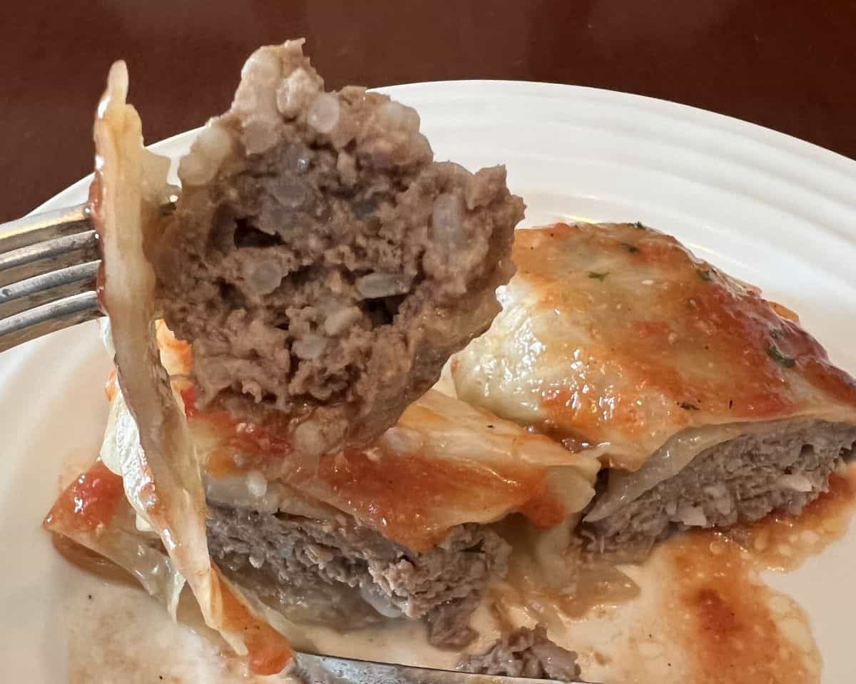 Closeup image of a fork with a bite of cabbage roll on it close to the camera with a plate of cabbage roll in the background.
