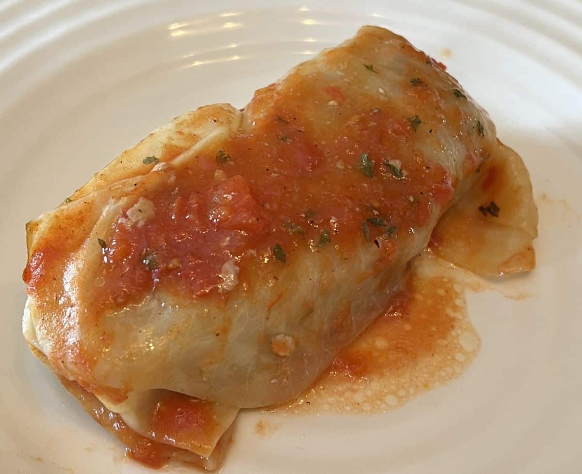 Closeup image of one cabbage roll served on a white plate after being heated.