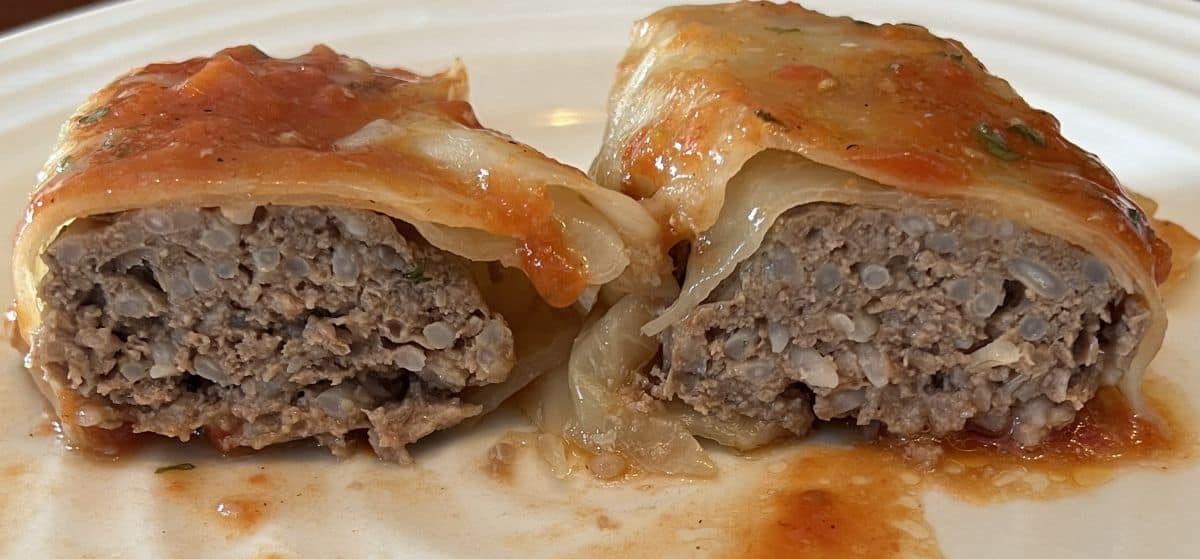 Image of one cabbage roll served on a white plate and cut in half so you can see the filling inside. 