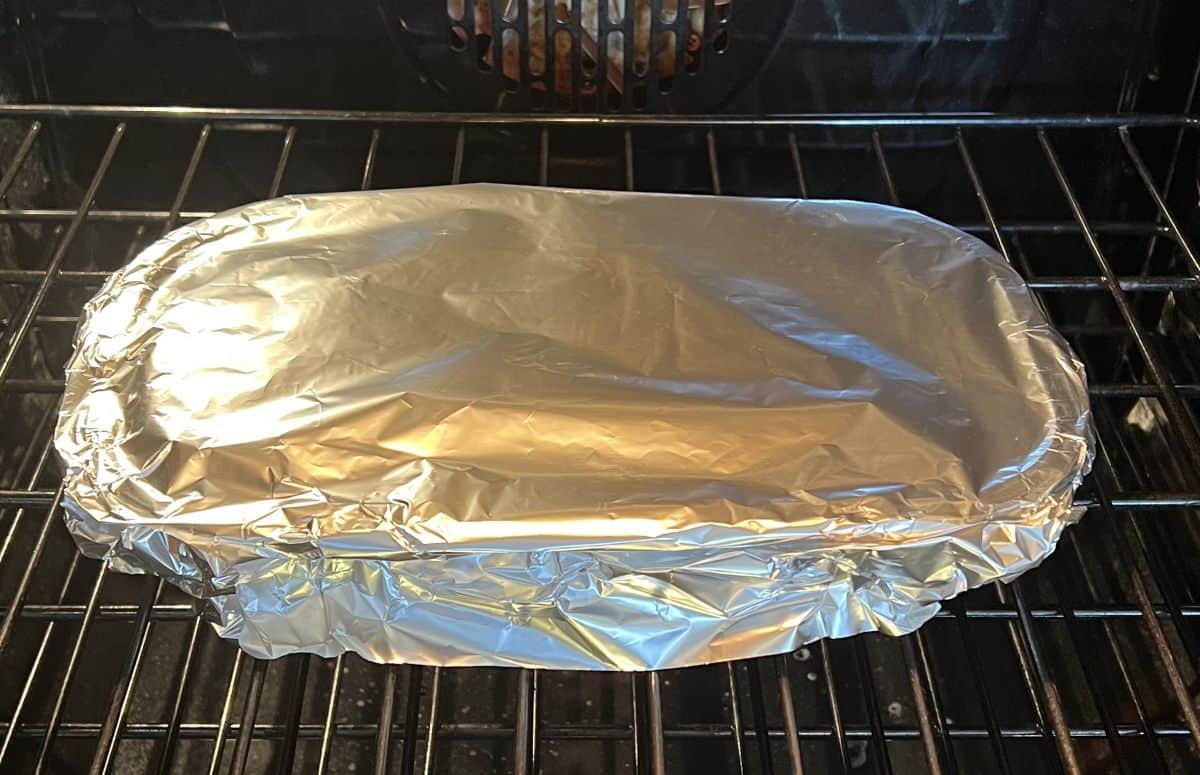 Image of the cabbage rolls heating in an oven with aluminum foil covering the tray.