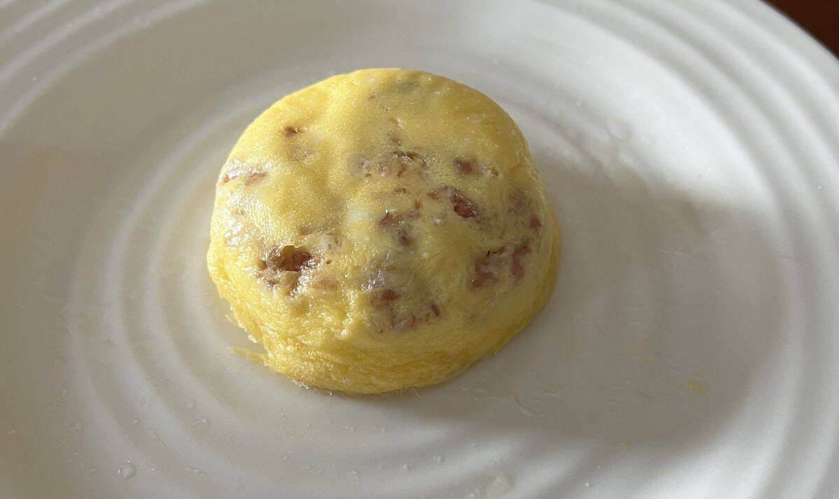 Top down image of one bacon & cheese egg bite served on a white plate.