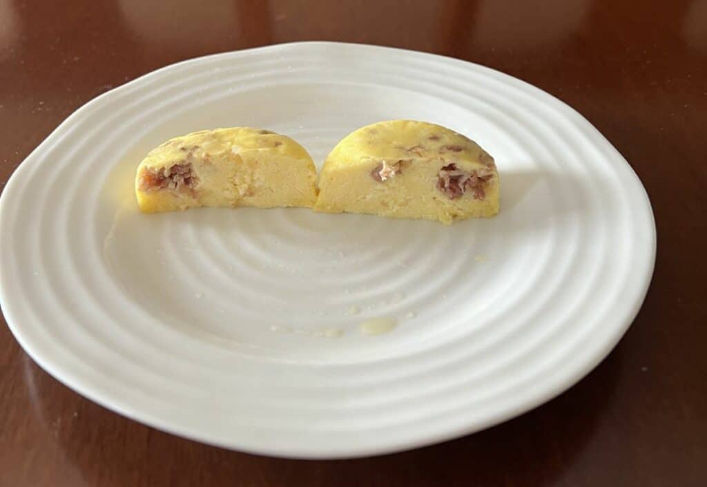 Image of one bacon & cheese egg bite cut in half so you can see the inside served on a white plate.