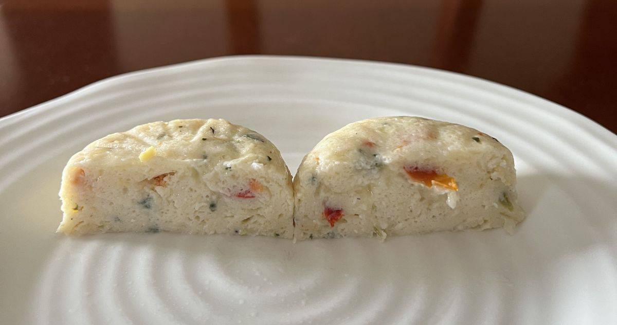 Image of one egg white with cheese & roasted red pepper egg bite cut in half so you can see the inside served on a white plate.