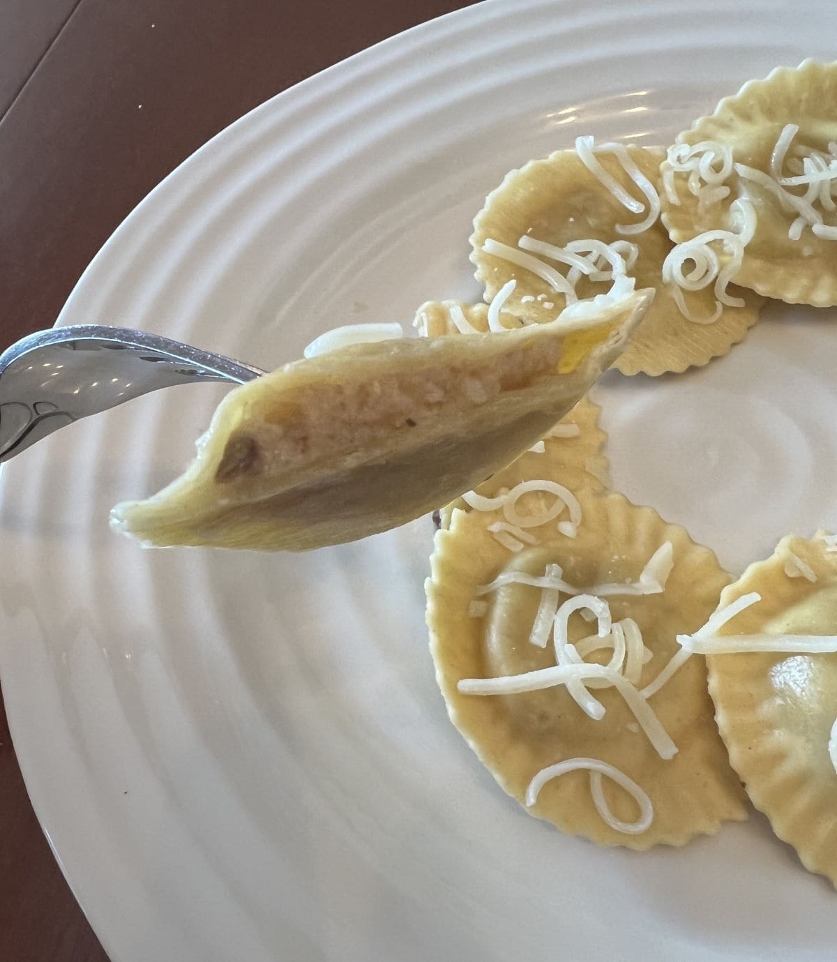 Closeup image of a fork with a ravioli that's been cut in half close to the camera so you can see what the filling looks like.