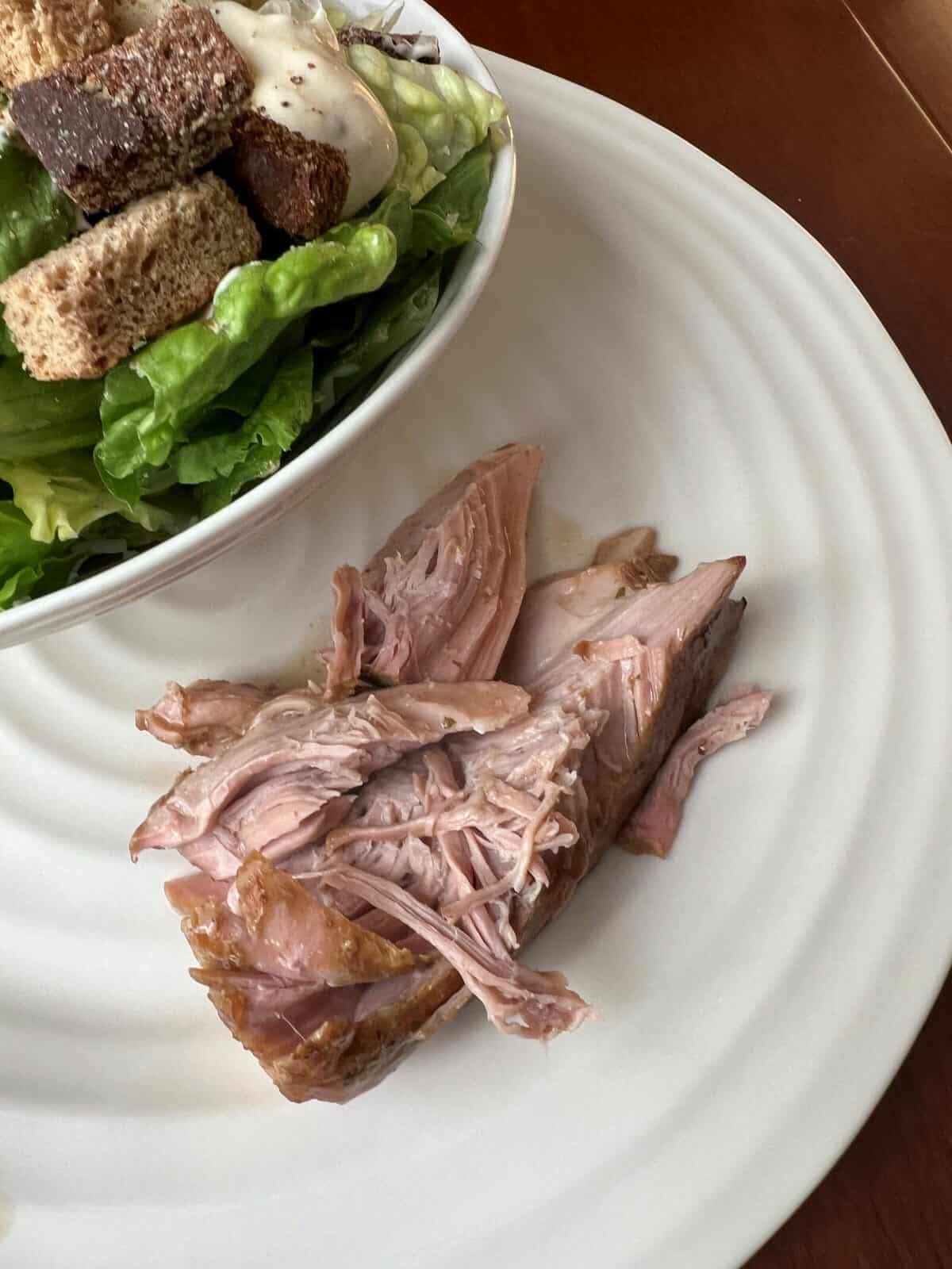 Top down image of a plate with pork roast and Caesar salad on it.