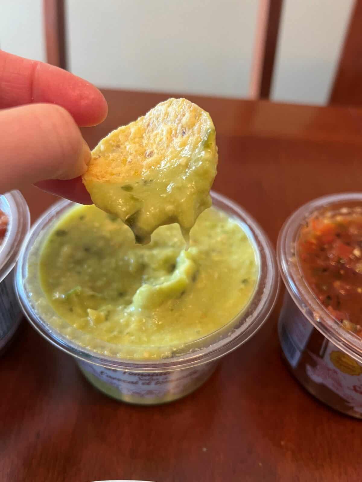 Image of a chip dipping avo tomatillo salsa from the container.