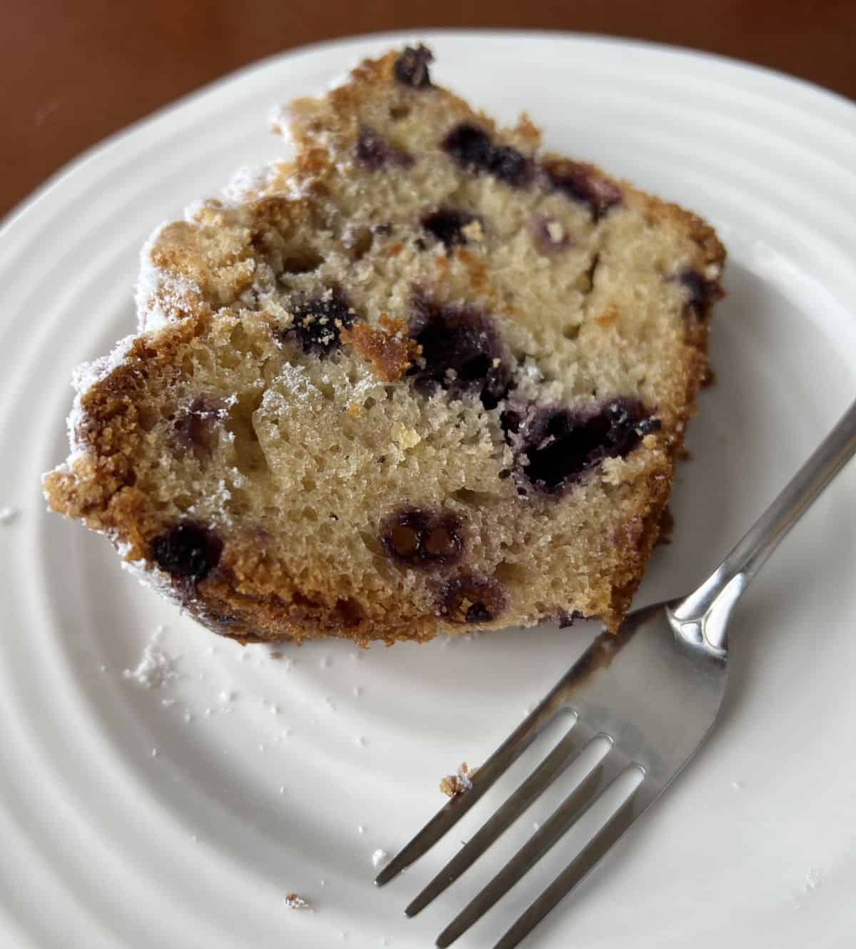 Image of a slice of lemon blueberry loaf served on a white plate.