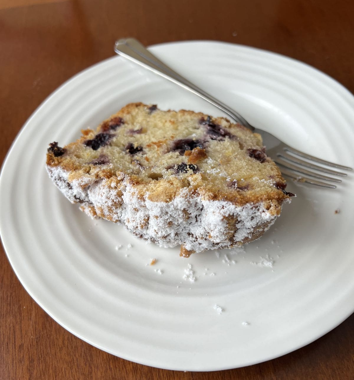 Image of a slice of lemon blueberry loaf served on a white plate beside a fork.