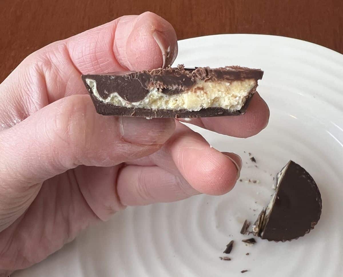 Closeup image of a hand holding one dark chocolate passion fruit cup cut in half so you can see the inside.