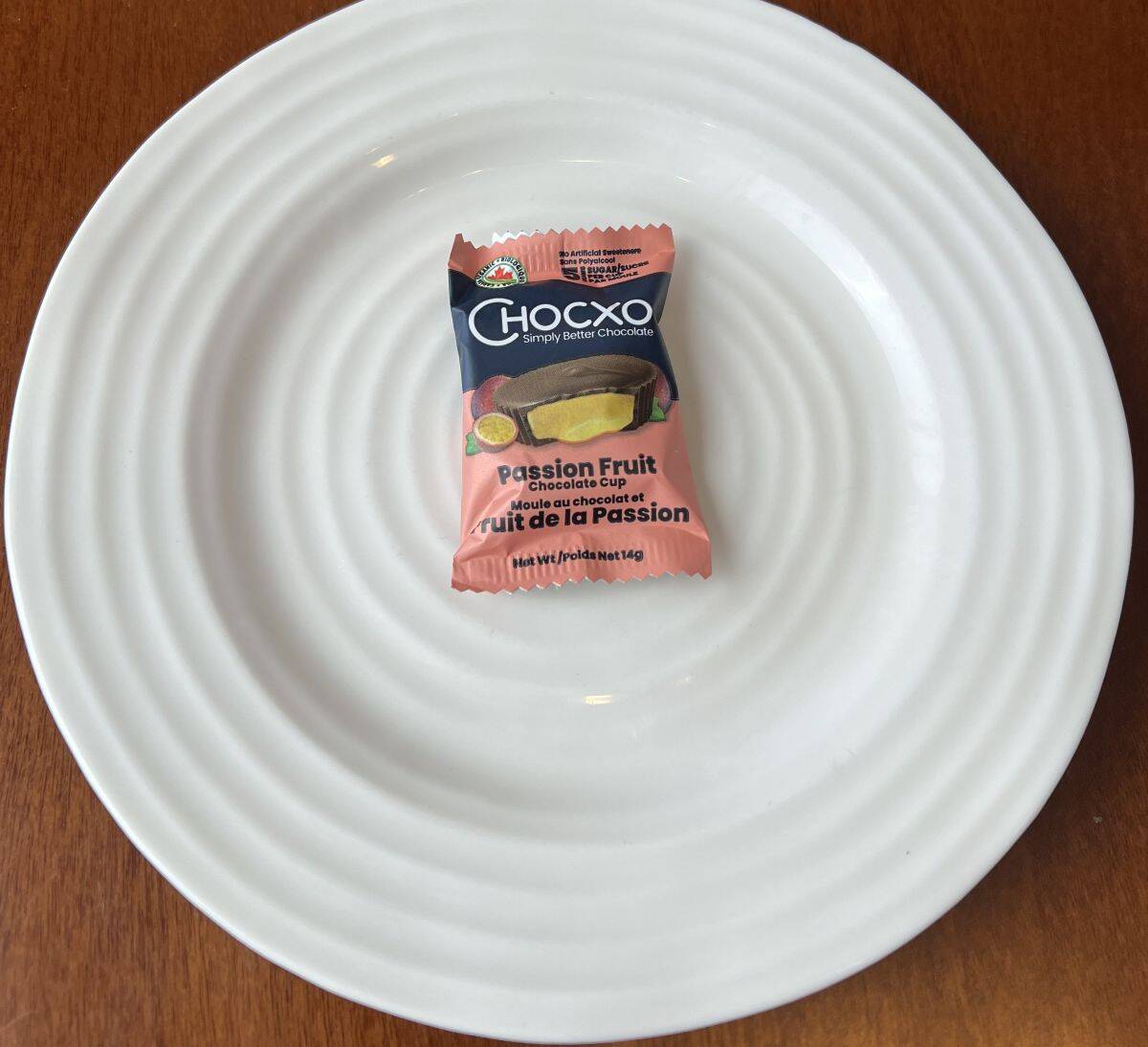 Image of one individually wrapped ChocXO passion fruit chocolate cup on a white plate. 