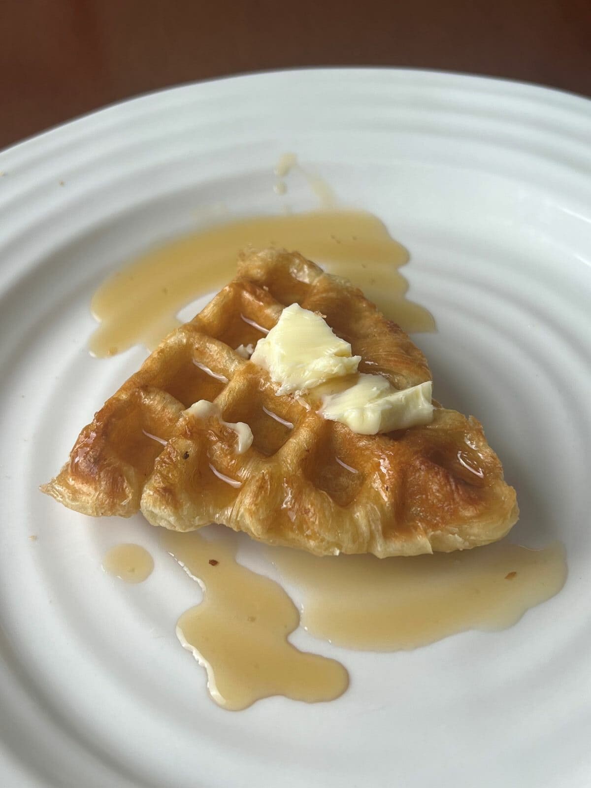 Closeup image of a Croffle served on a white plate with butter and syrup. 