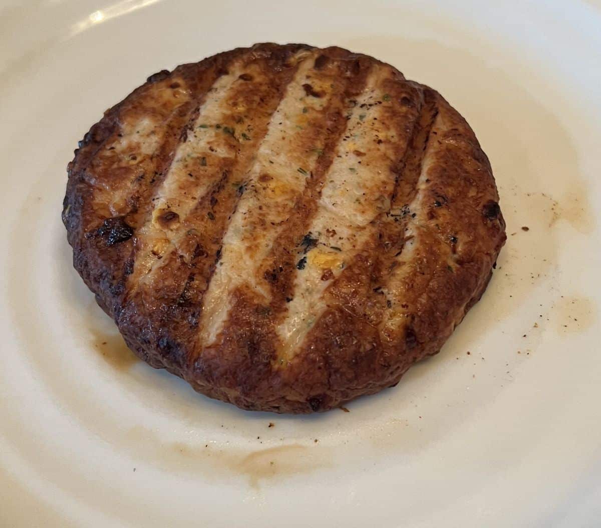 Top down image of one cooked Connie's Kitchen Caramelized Onion & Cheese chicken burger served on a white plate. 