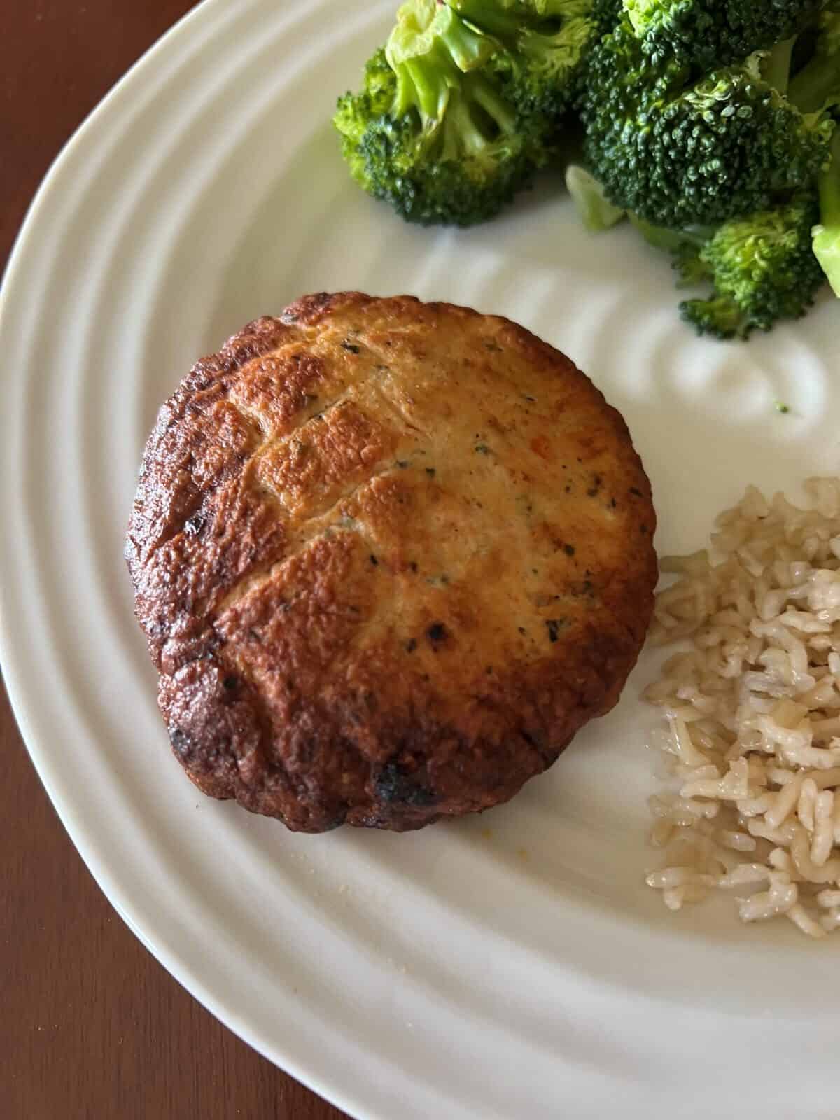 Top down image of a roasted red pepper chicken burger served on a white plate beside rice and broccoli. 