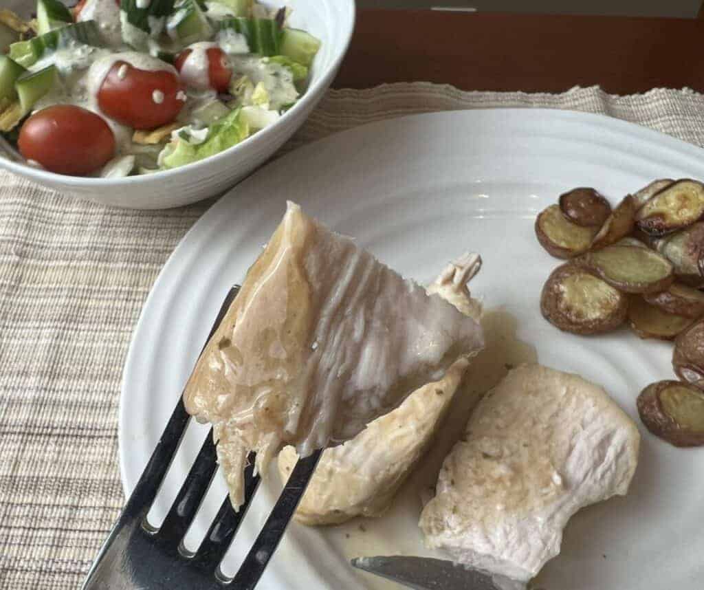 Image of a fork with cooked turkey breast on it hovering over a plate of turkey and potatoes.