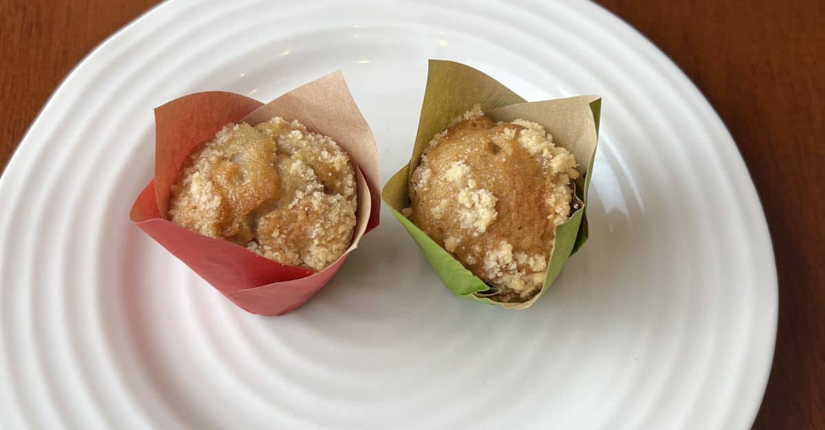 Image of two muffins served on a white plate one is in a red wrapper and one is in a green wrapper.